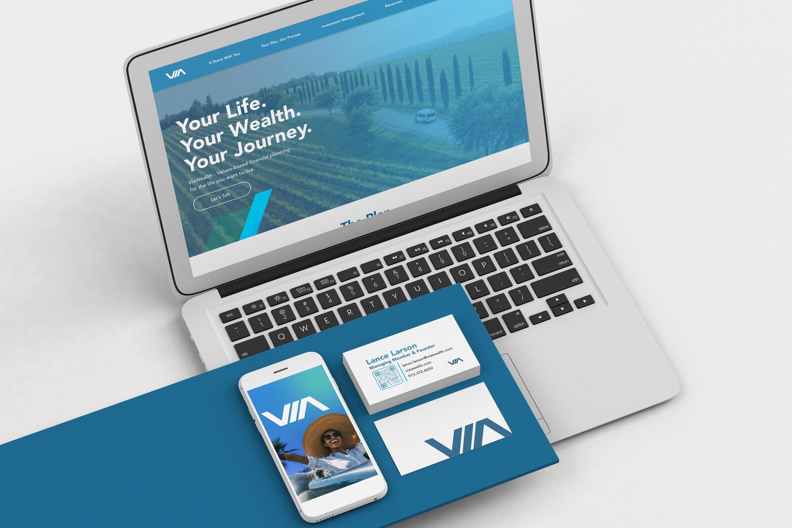 ViaWealth site design on a laptop beside app screens and business cards in brand blue